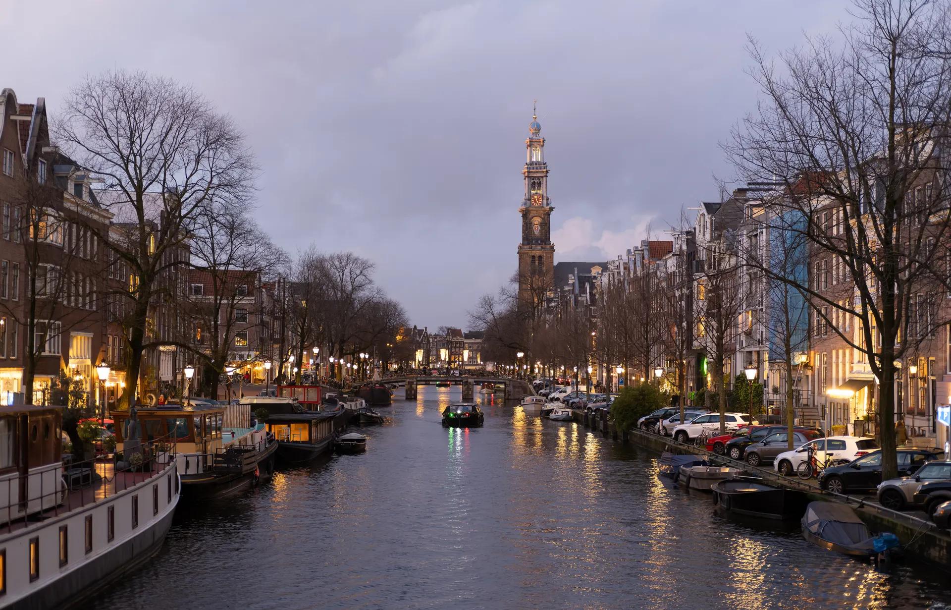 Prinsengracht canal lined with houseboats and the Westerkerk tower at dusk
