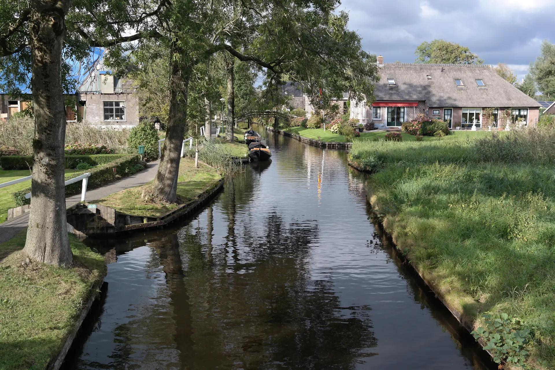 A narrow canal in Giethoorn lined with grass banks, trees and thatched houses