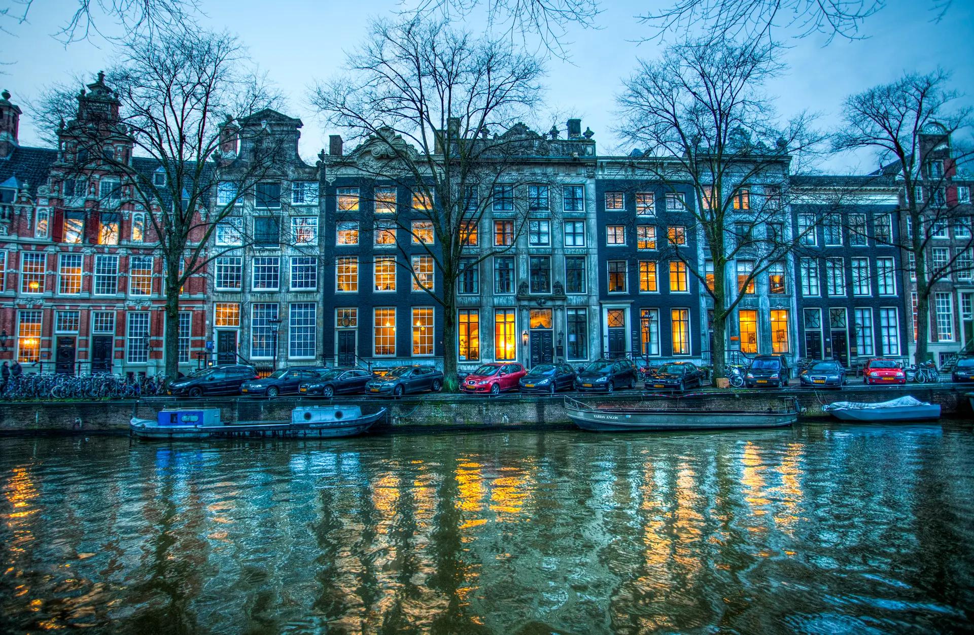 Lit windows of canal houses on the Herengracht reflected in the water at blue hour
