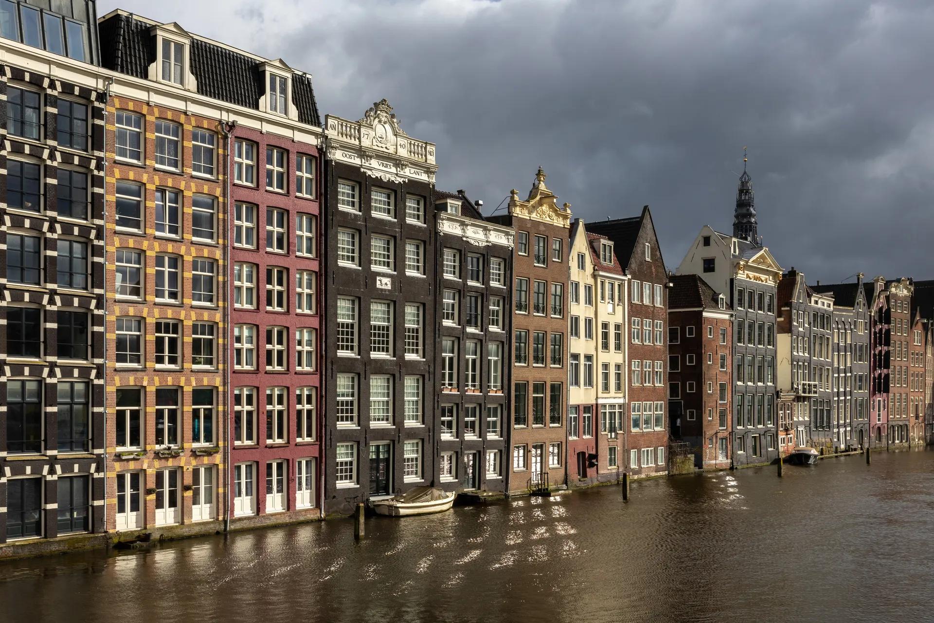 Colourful canal houses on the Damrak with the bell tower of the Oude Kerk behind
