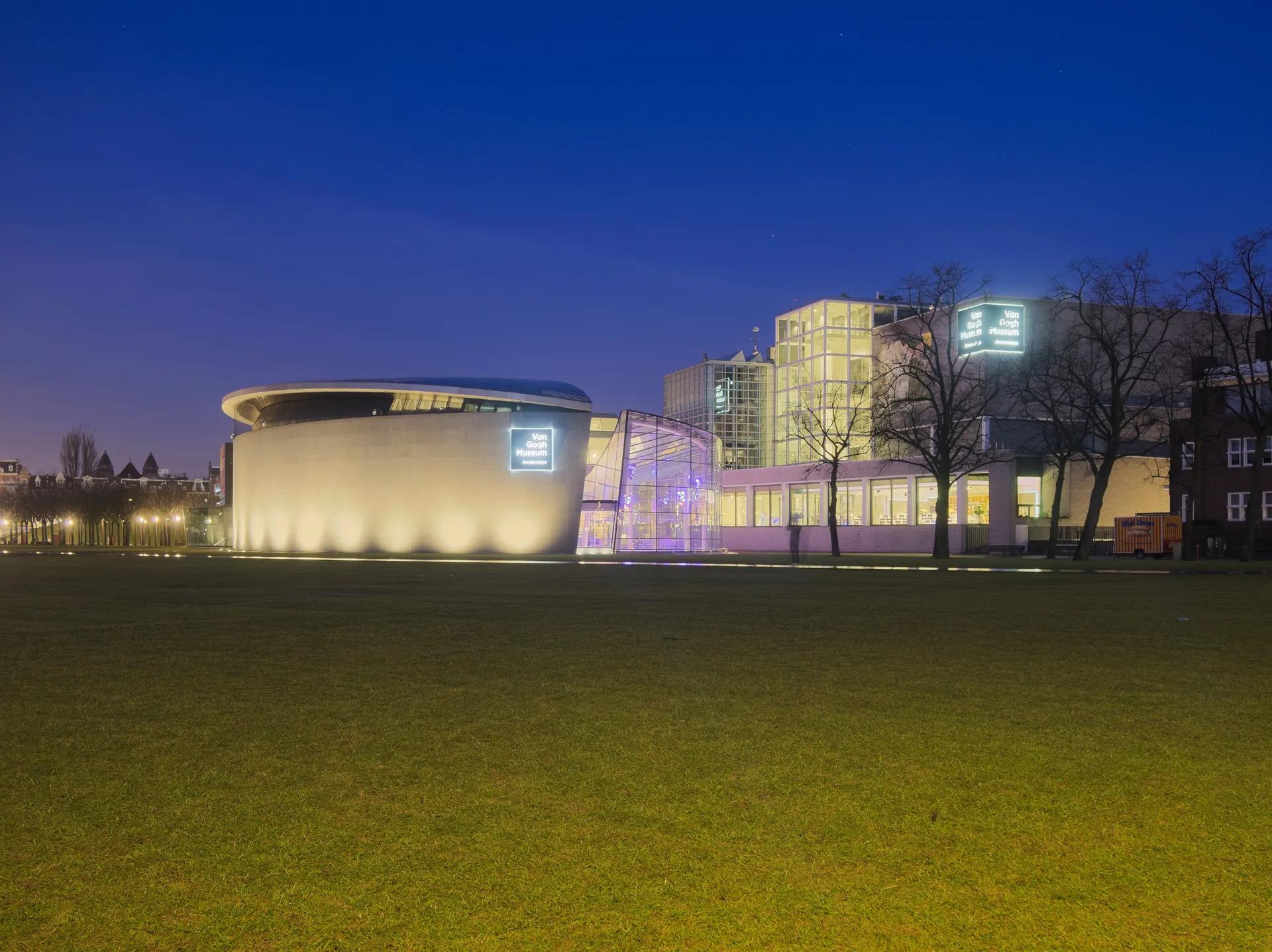 The oval wing of the Van Gogh Museum lit up across the Museumplein lawn at dawn