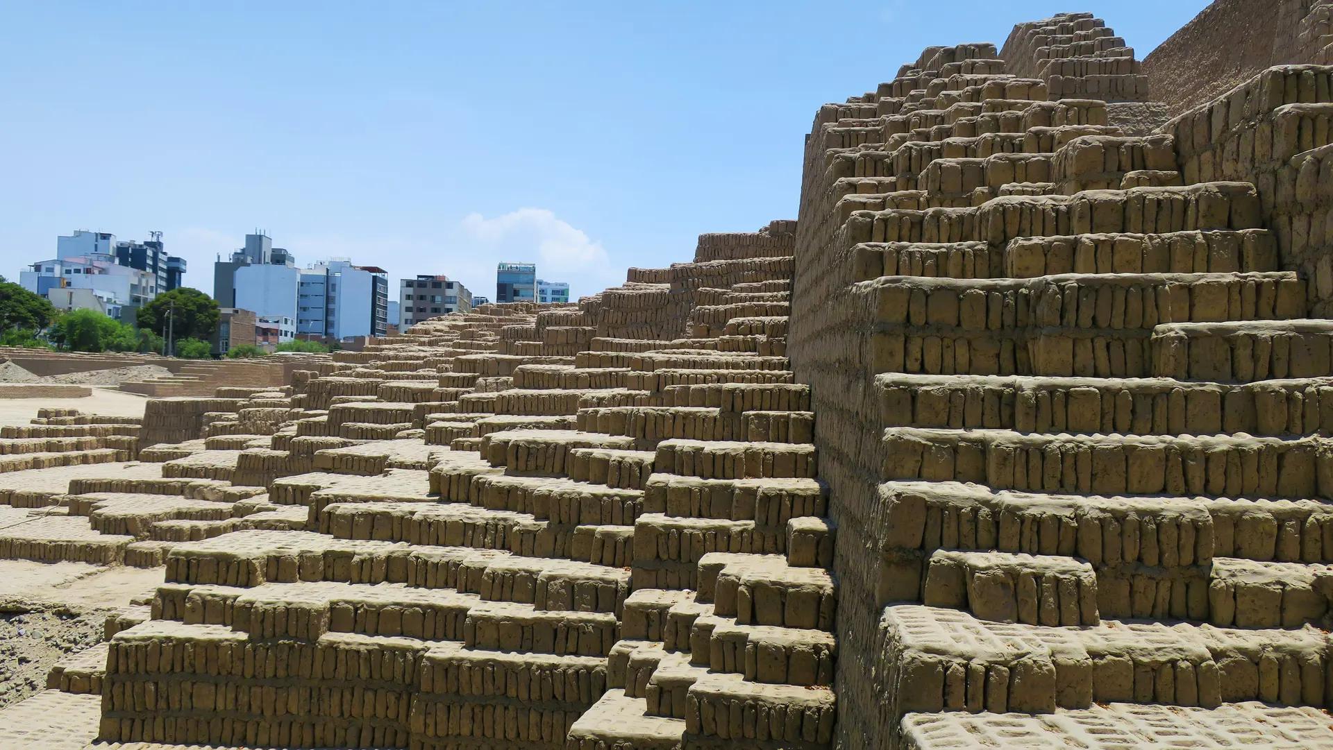 Stepped adobe walls of Huaca Pucllana pyramid with Miraflores buildings behind