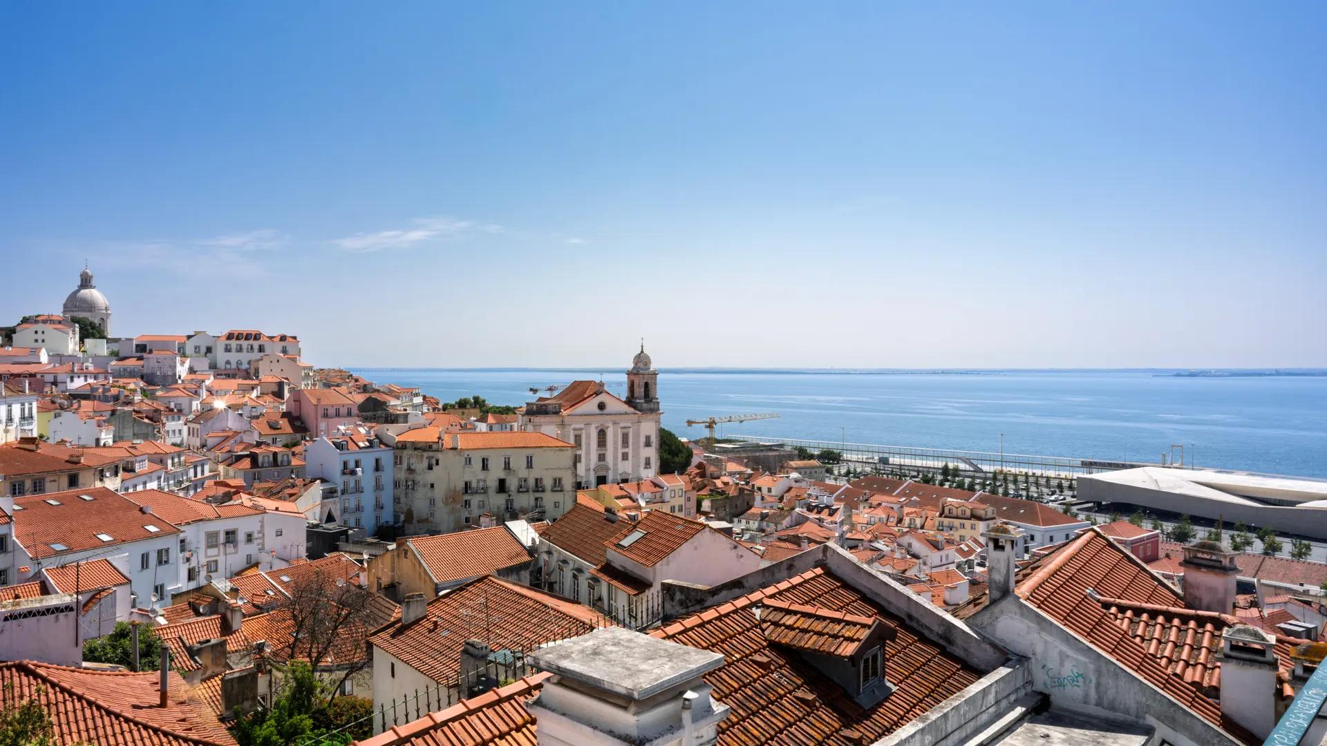 Terracotta rooftops of Alfama sloping down to the Tagus, with the National Pantheon dome