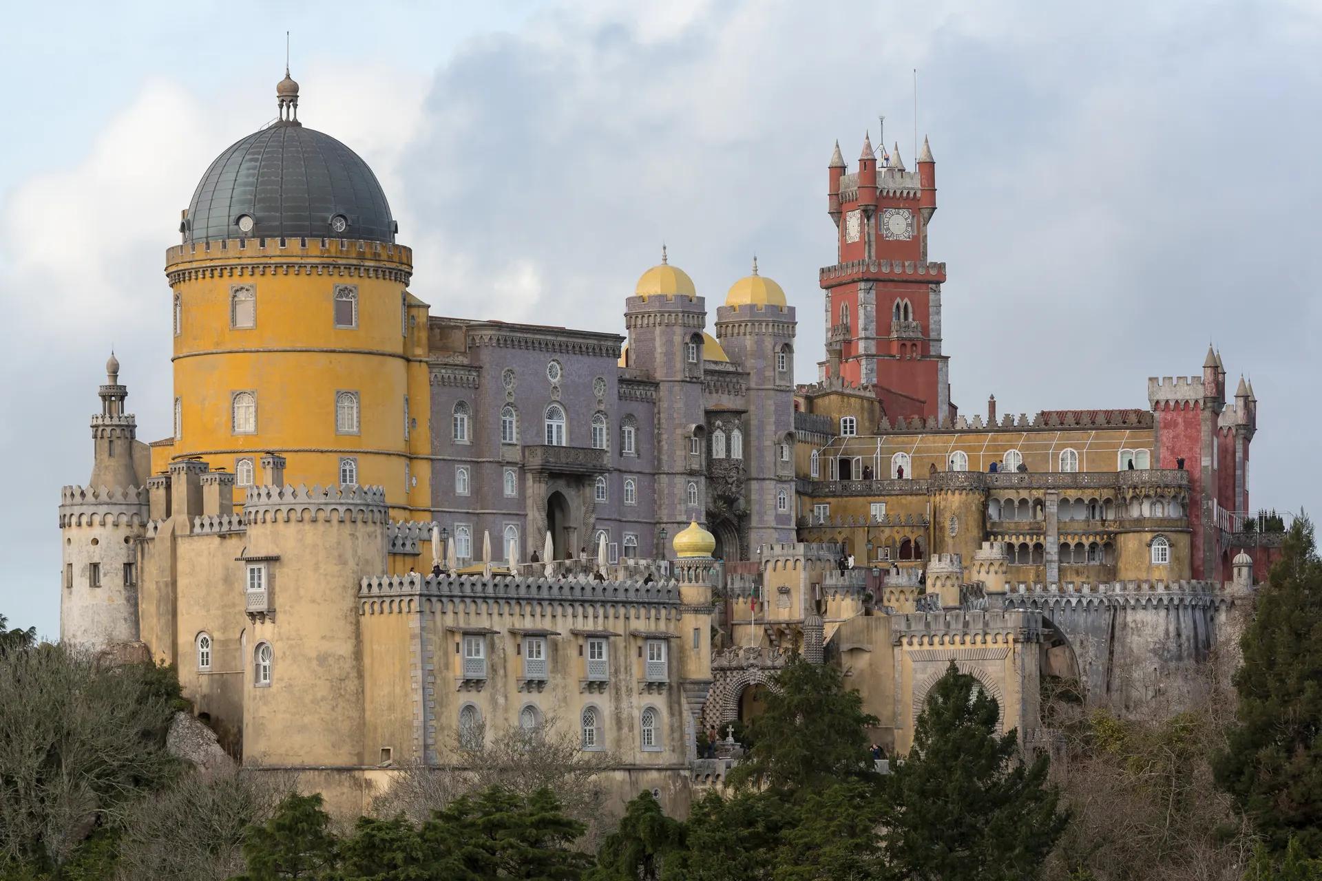 Yellow, grey and red towers and domes of Pena Palace above the trees