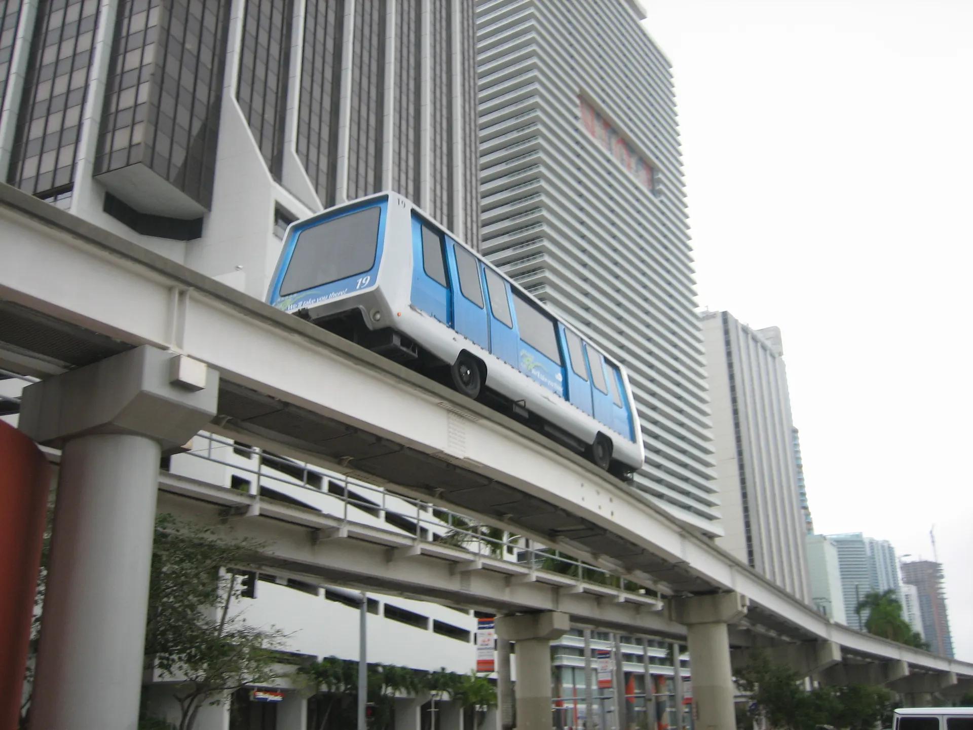 Blue and white Metromover car on its elevated guideway between downtown towers