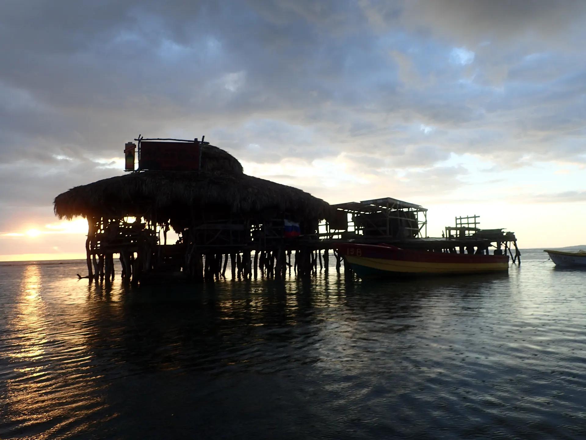 Floyd's Pelican Bar, a wooden bar on stilts in the sea, silhouetted at sunset
