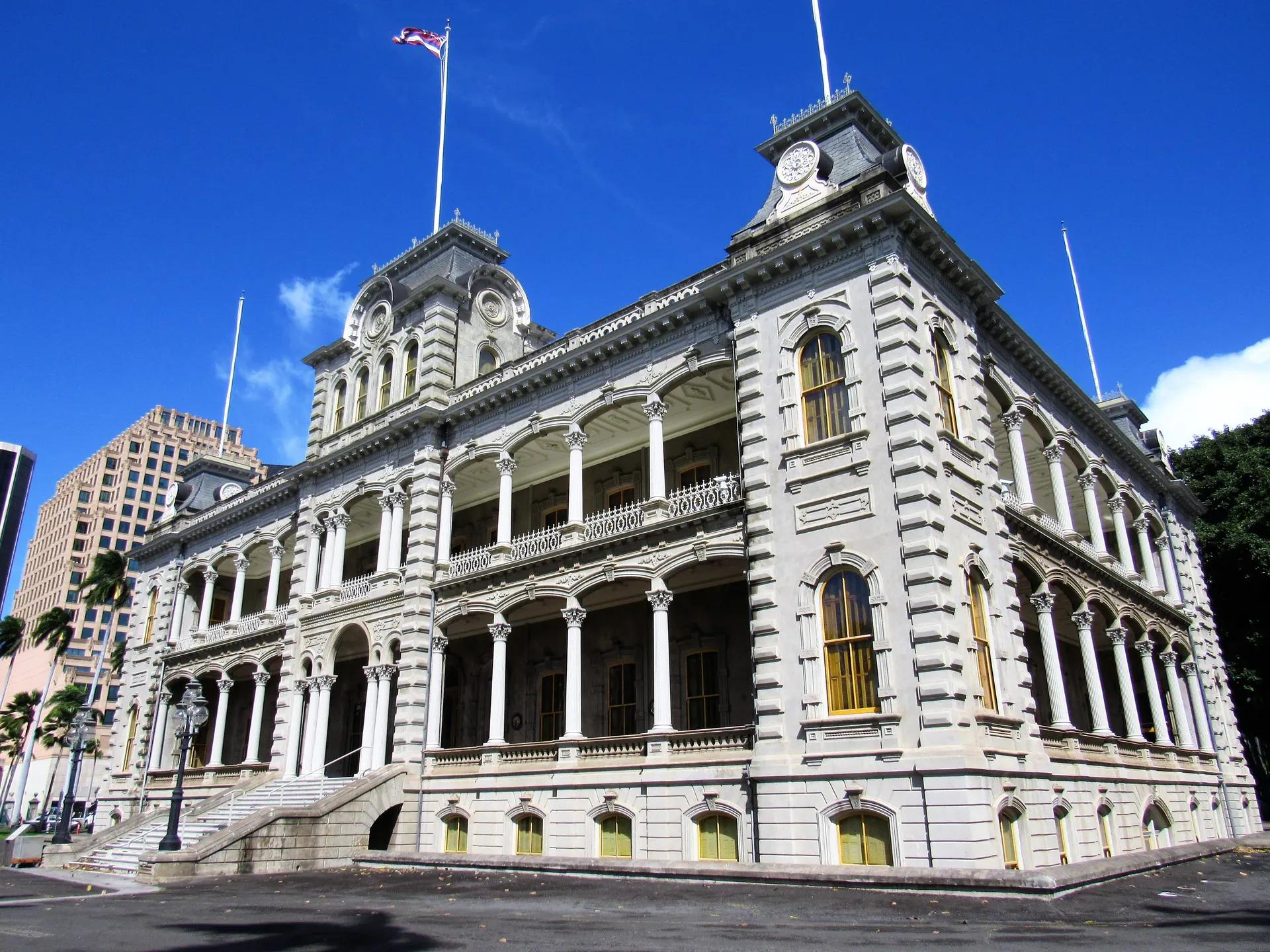 The stone facade and verandas of Iolani Palace under a blue sky