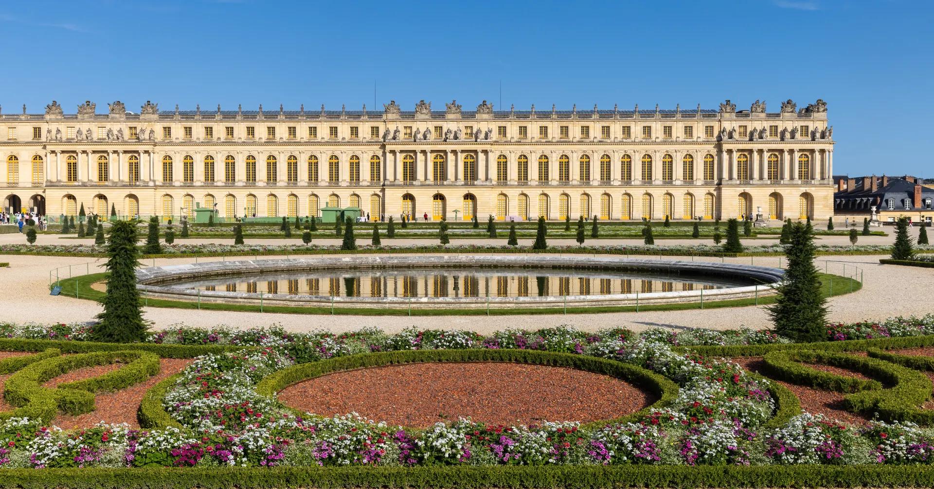 Garden façade of the Palace of Versailles behind the Parterre du Midi flowerbeds and a round pond