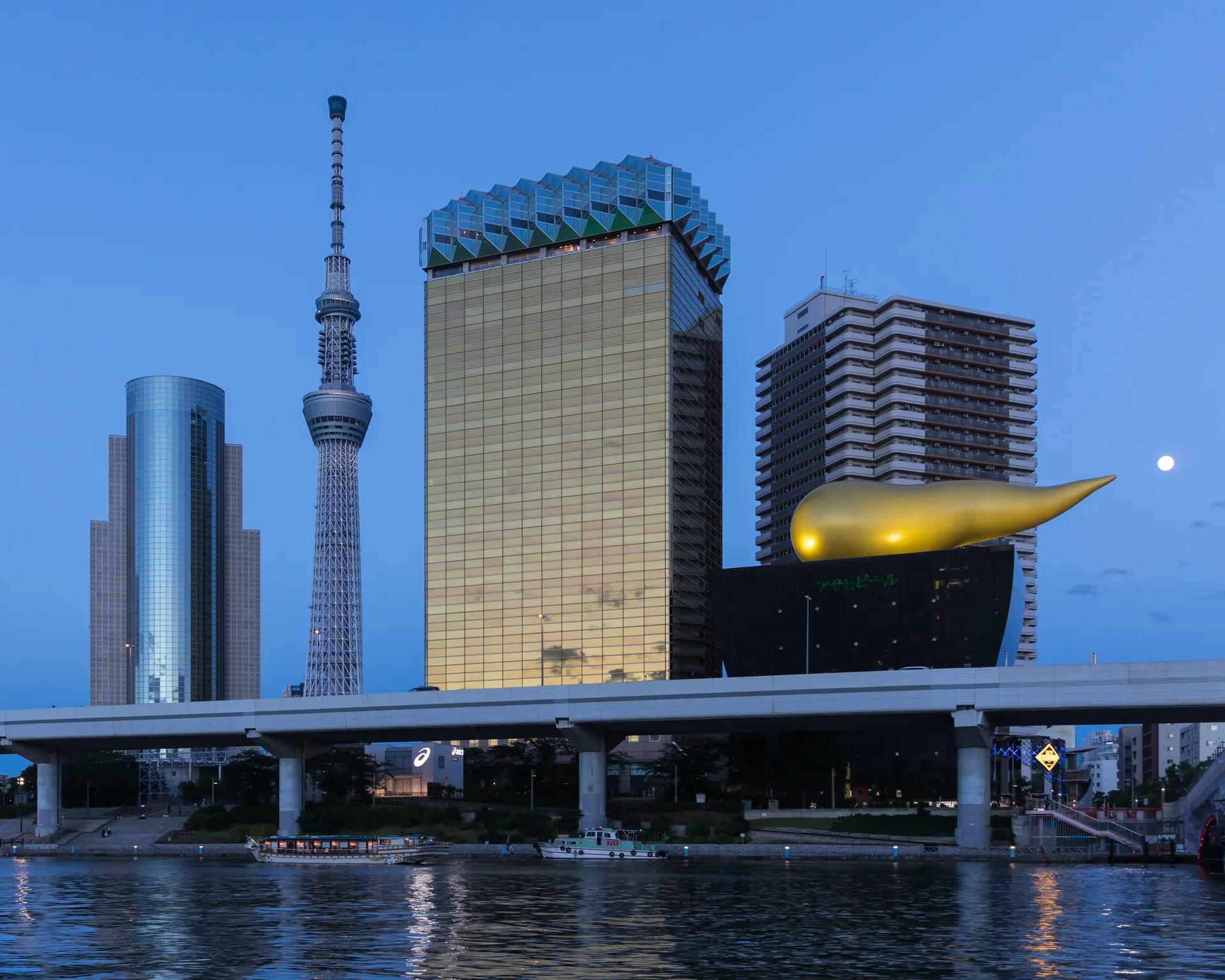 Tokyo Skytree rising behind the Asahi Breweries buildings on the Sumida River at blue hour