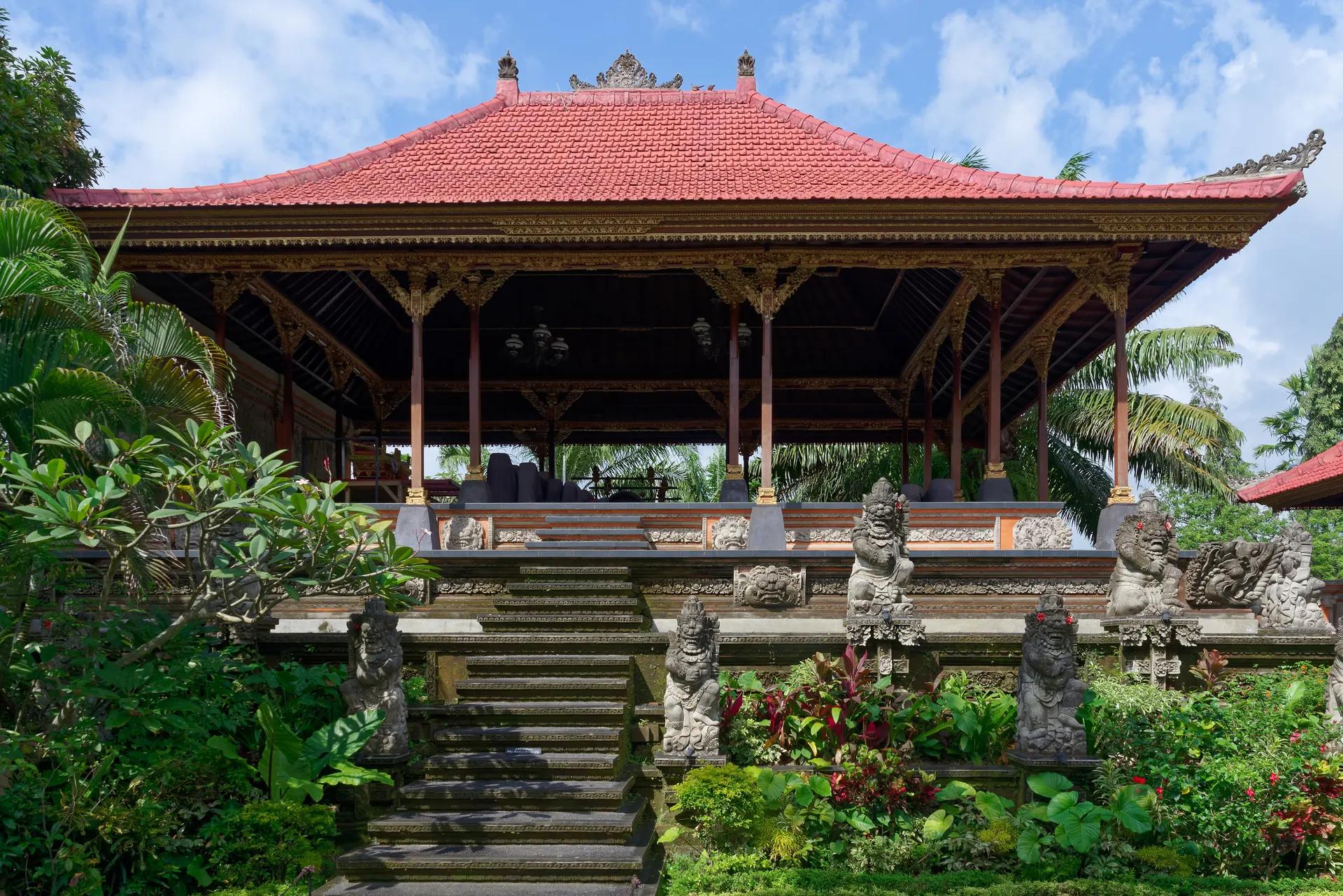 Pavilion with red tiled roof and stone statues at Ubud Palace