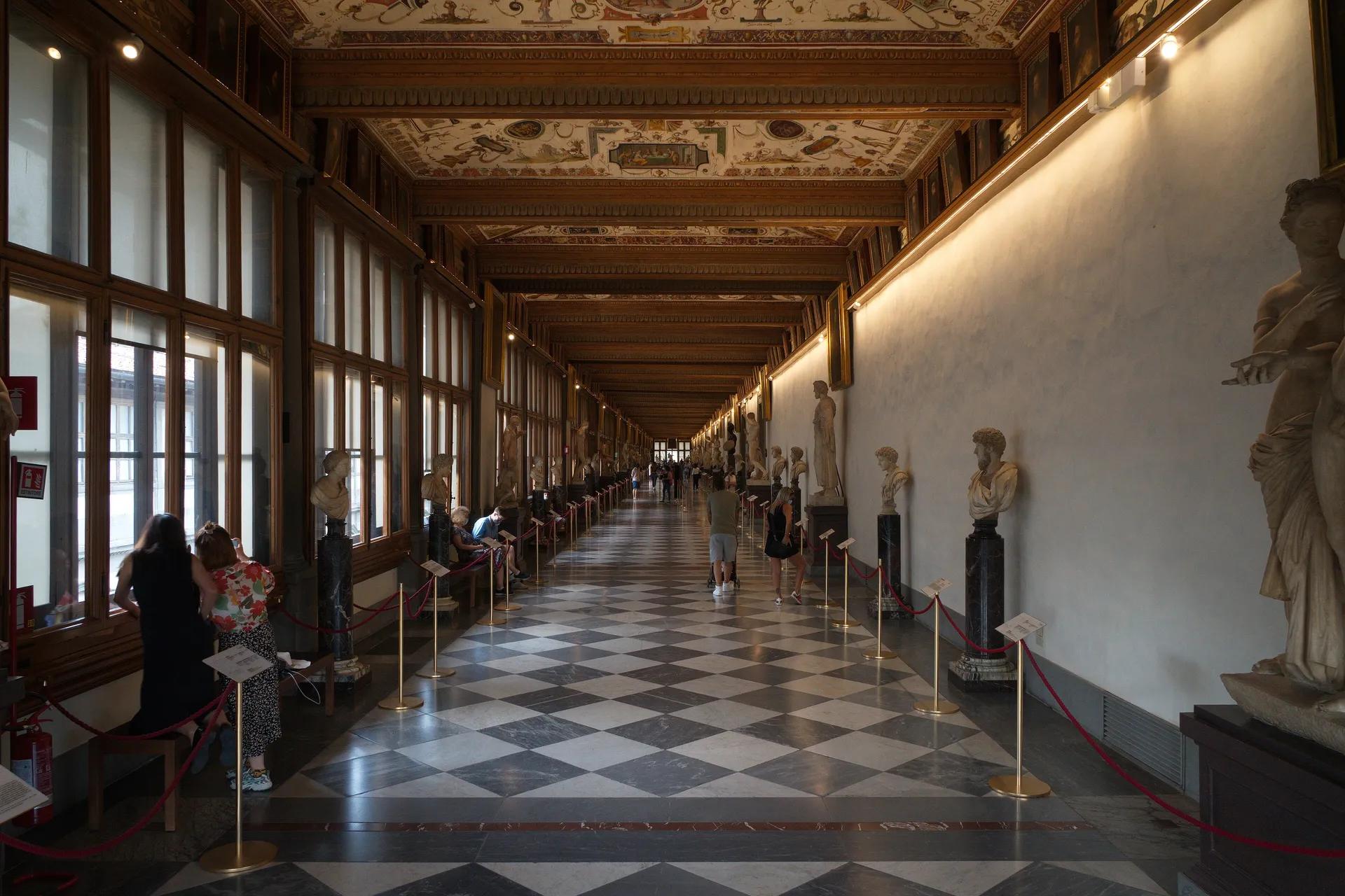 Long corridor of the Uffizi Gallery lined with ancient busts and statues under a painted ceiling